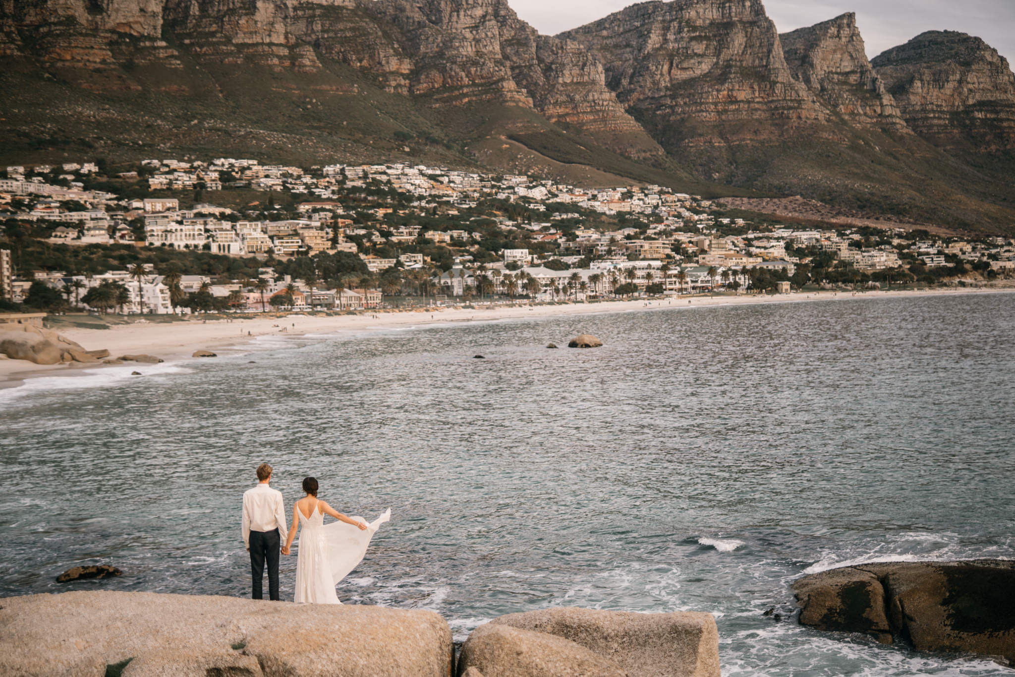 A bride and groom at a destination wedding photography shoot on a rocky beach.