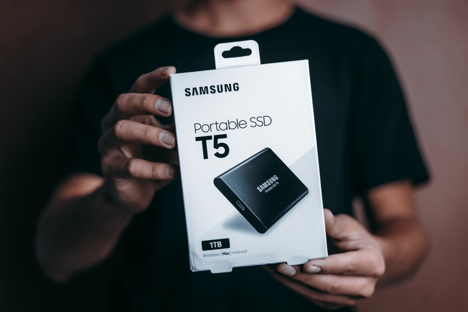 A photographer holding a Samsung 1TB SSD for photo and video storage.