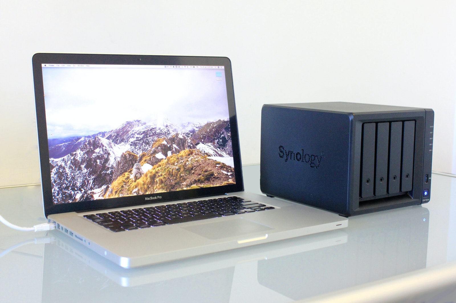 MacBook Pro laptop with a Synology NAS storage unit set up on a home office desk.