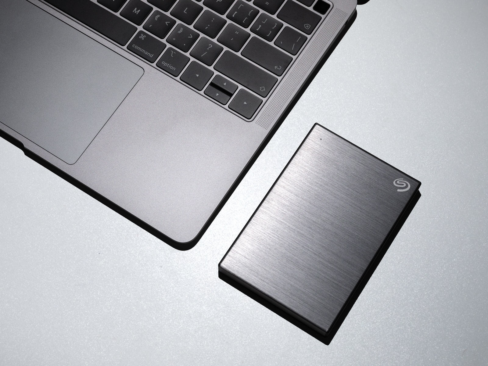 A portable Seagate SSD next to a laptop on a photographer’s home desk.