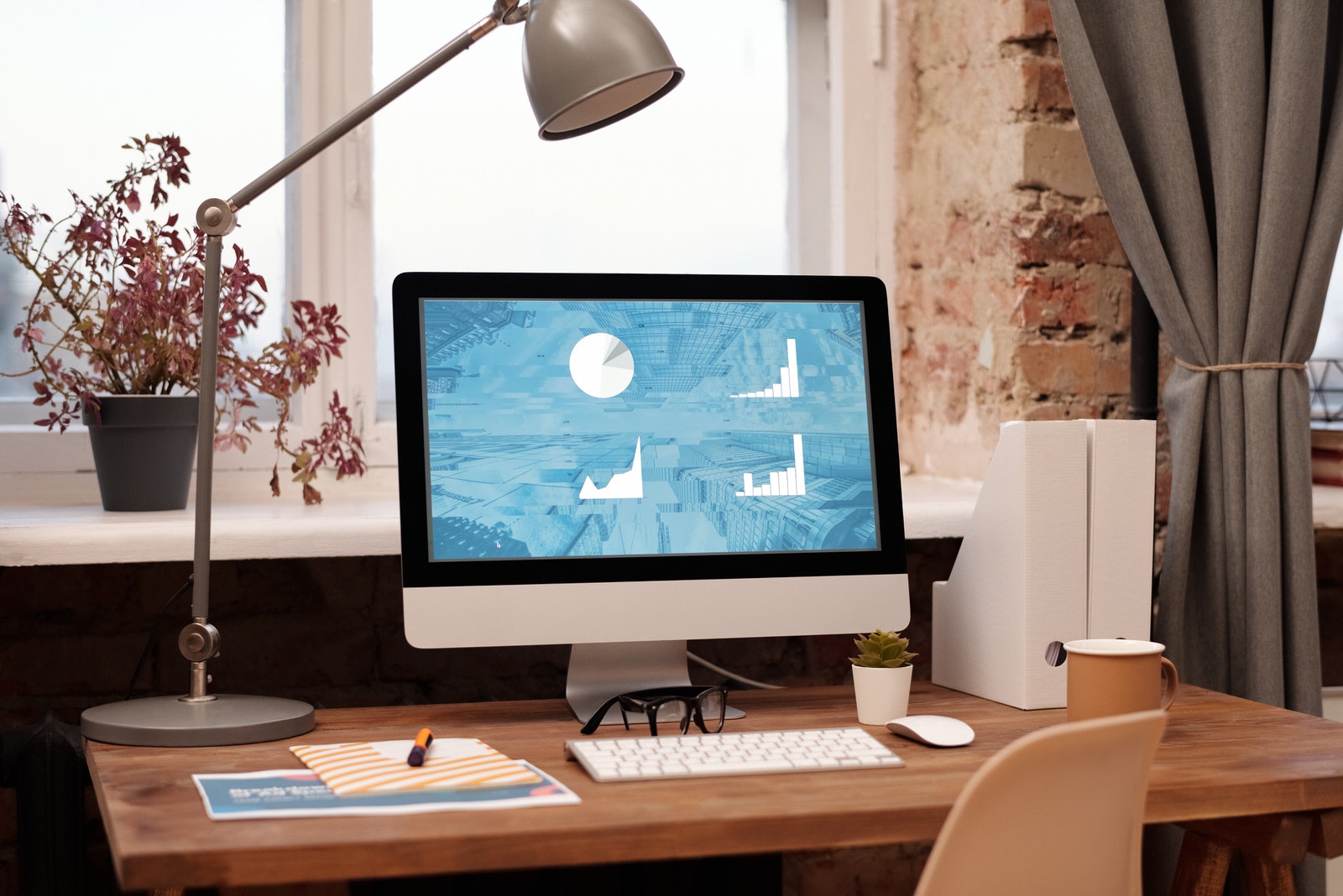 A photographer’s home office desk with a computer, keyboard, lamp, and office supplies.