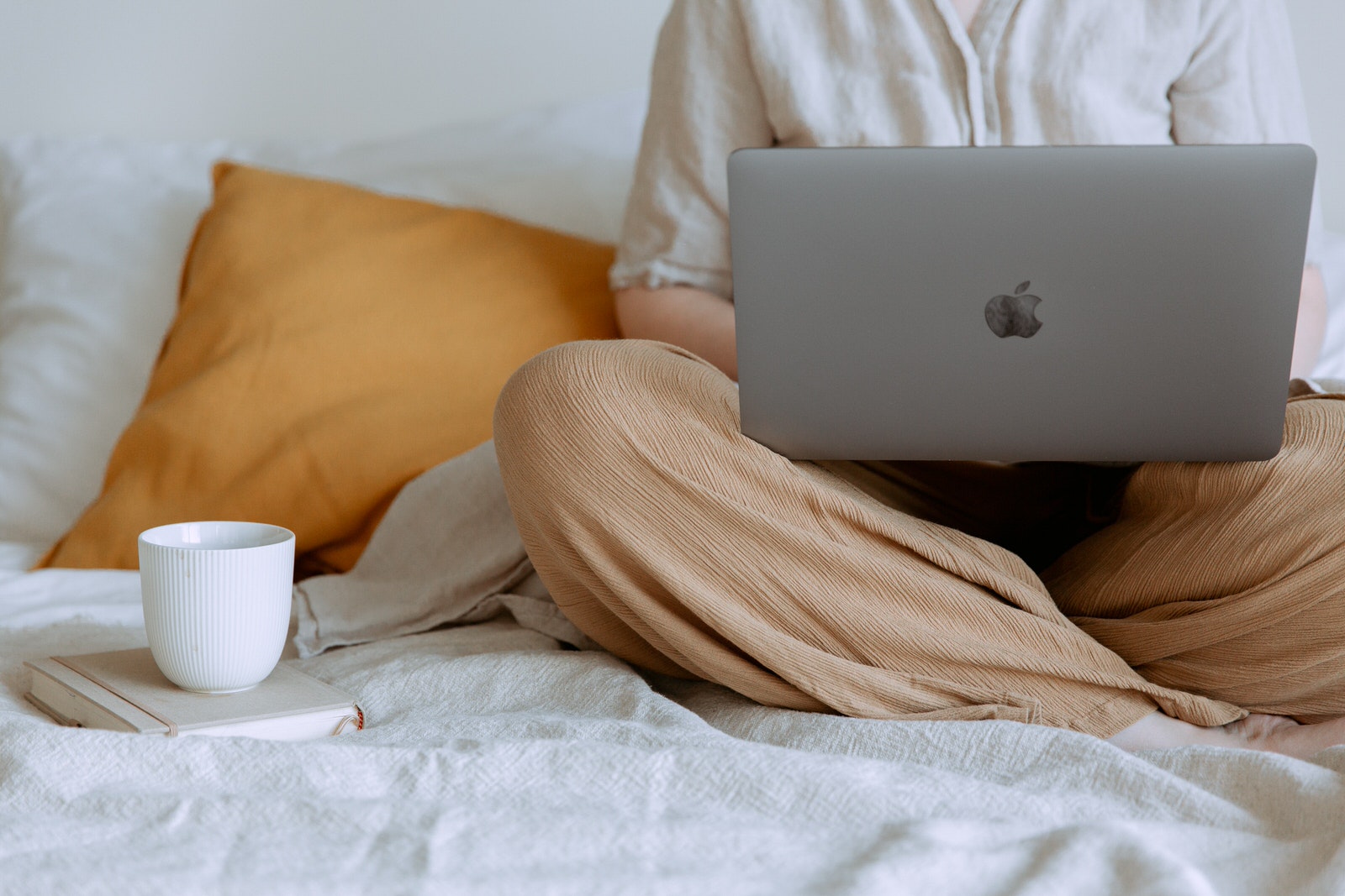 A photographer using Apple MacBook at home on a bed, uploading photos and files on the cloud.