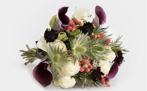 Elegant bouquet featuring white roses, deep purple calla lilies, red berries, and greenery against a white background, ideal for weddings or sophisticated events.