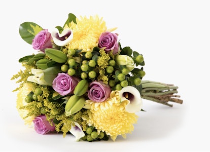 Bright bouquet of flowers with yellow blooms, purple roses, and green foliage tied with twine against a clean white background.