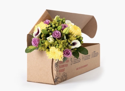Open cardboard box with a vibrant floral arrangement featuring yellow chrysanthemums, pink roses, and purple accents on a white background.