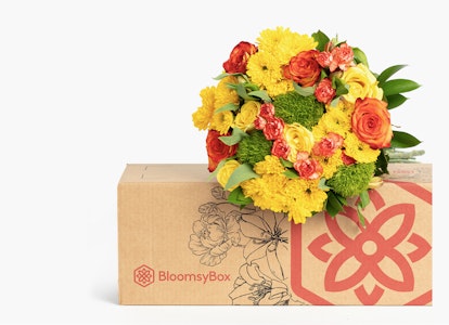Vibrant bouquet of yellow and red roses with greenery in a BloomsyBox, set against a neutral background, showcasing fresh flower delivery service.