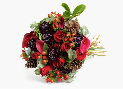 Vibrant bouquet of red roses and berries with pine cones and green leaves, tied with twine, set against a white background, perfect for festive occasions.
