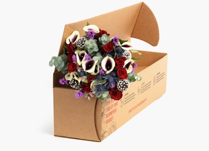 Bouquet of colorful flowers with red roses and white lilies emerging from an open cardboard box on a neutral background, showcasing a flower delivery service.