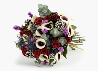 Elegant bridal bouquet featuring a mix of calla lilies, red roses, purple accents, and green foliage tied together, isolated on a white background.