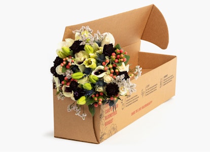 Elegant bouquet of mixed flowers with white, black, and green colors carefully placed in an open cardboard box against a clean white background, ready for delivery.