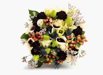 Elegant bouquet featuring yellow lilies, white calla lilies, and red berries with green foliage and small white flowers, arranged against a white background.