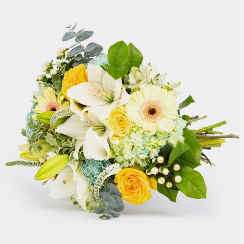 Bouquet of assorted flowers featuring yellow roses, white lilies, and daisies with green foliage on a white background, showcasing fresh and vibrant floral arrangement.