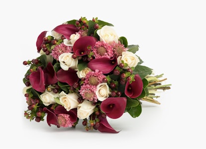 A beautiful bouquet featuring deep red calla lilies, white roses, and pink accents arranged with greenery against a white background, perfect for weddings or special occasions.