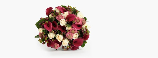 Elegant bouquet featuring deep red calla lilies and roses, accented with smaller white roses and greenery, presented against a clean white background.