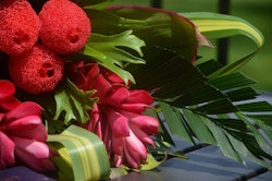 Vibrant bouquet featuring red tulips and unique red sponge-like flowers, complemented by green tropical leaves, arranged elegantly on a reflective surface.