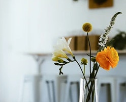 Elegant glass vase showcasing a delicate arrangement of wildflowers, including a bright yellow bloom, set against a soft-focus white interior background.