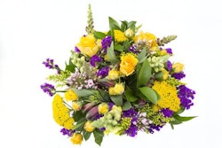 A vibrant bouquet featuring yellow roses, purple accent flowers, green foliage, and various mixed blooms against a white background, perfect for a special occasion.