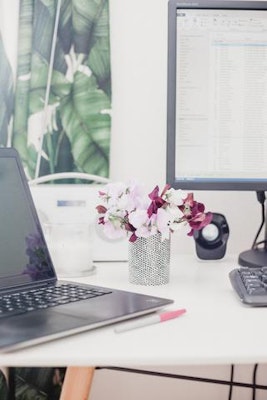 A stylish workspace featuring a sleek laptop, vibrant flower vase, and dual monitors.