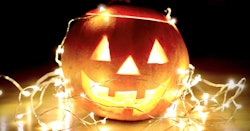 Illuminated jack-o'-lantern with a carved smiling face wrapped in twinkling string lights on a wooden surface, creating a festive and spooky Halloween atmosphere.