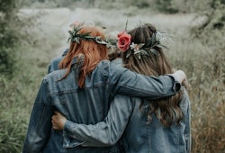 Two people wearing floral crowns and denim jackets embracing in a field, showcasing friendship and bohemian style amidst a natural backdrop.