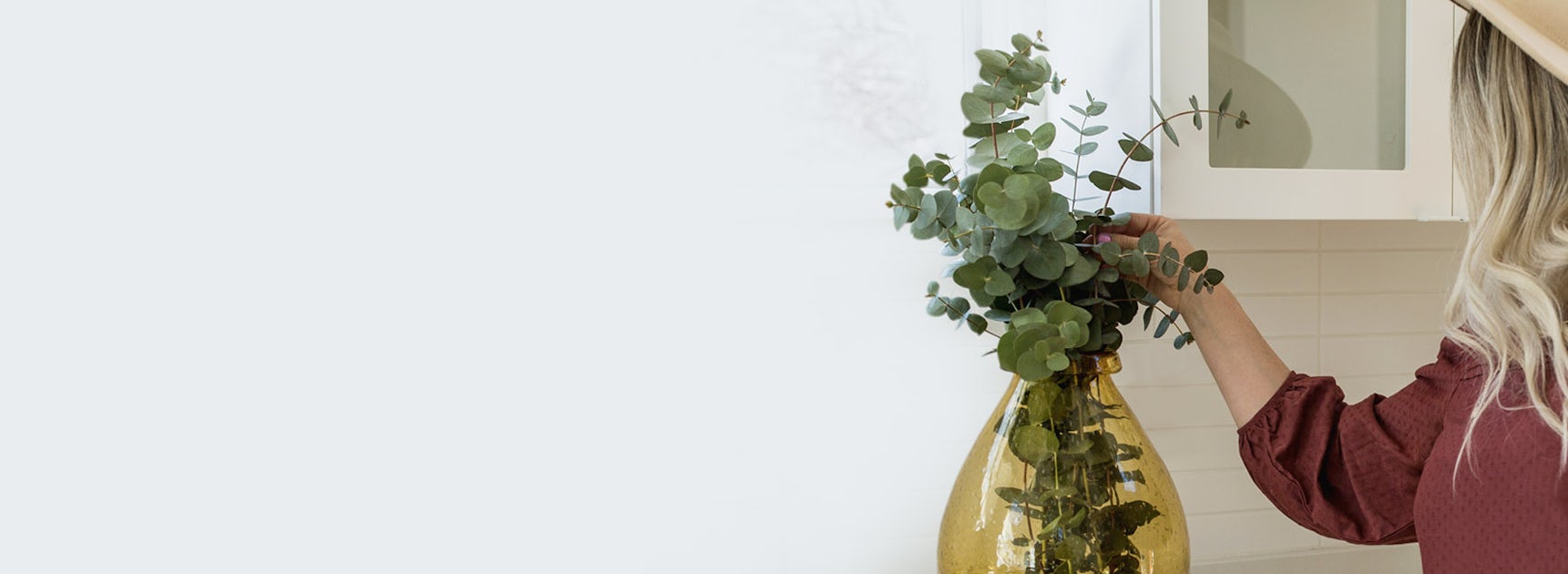 A stylish woman arranges eucalyptus stems in a chic glass vase at home, enhancing interior decor.