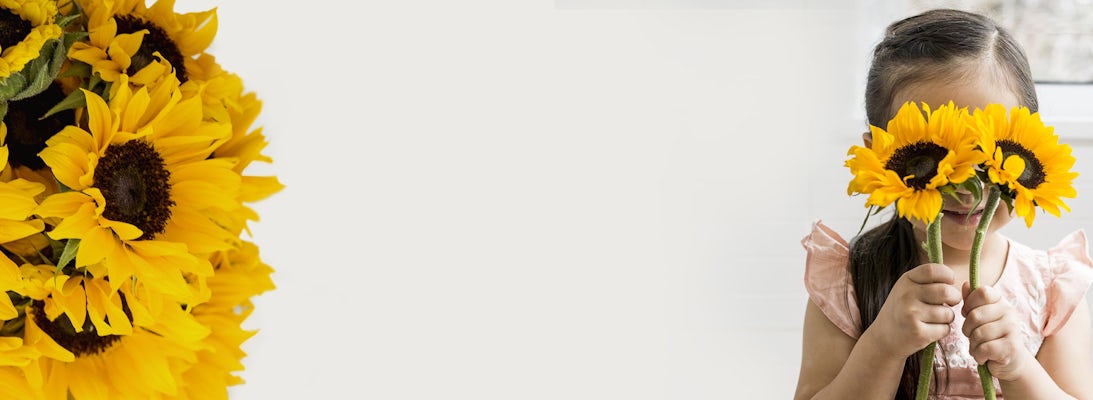 Cheerful young girl holding vibrant sunflowers, expressing joy and playfulness in a sunny setting.