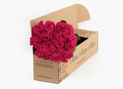A box of vibrant pink roses with lush green leaves packaged in a cardboard box designed for flower delivery, set against a neutral background.