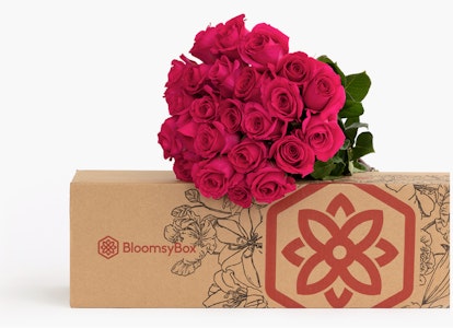 A vibrant bouquet of fresh red roses arranged elegantly on top of a BloomsyBox with a decorative flower logo, displaying a perfect gift option or subscription service.