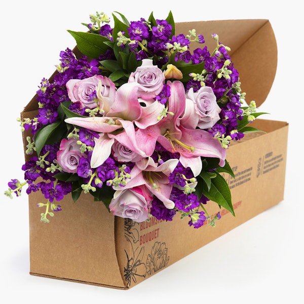 Vibrant floral bouquet featuring pink lilies and roses with purple accents, freshly packaged in a brown cardboard presentation box, ready for delivery.