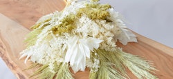Fresh white flower arrangement with baby's breath and greenery on a natural wooden surface, conveying a minimalist and organic aesthetic for home decoration.