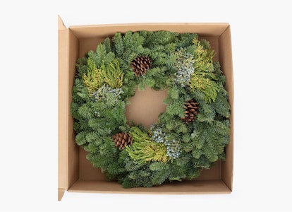 Fresh holiday wreath with lush greenery and pine cones neatly packaged in a cardboard box, viewed from above, perfect for seasonal decoration.