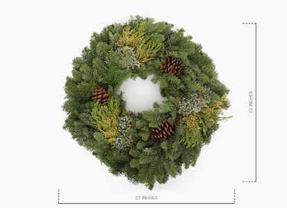 Green holiday wreath with pine cones and various evergreen foliage on a white background, measuring 12 inches in diameter.