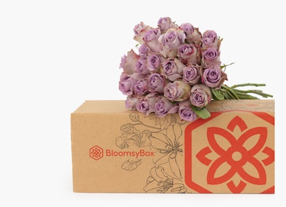 A bouquet of delicate pink roses atop a floral-themed BlossomsBox with a striking red flower logo, against a clean white background, representing freshness and elegance.