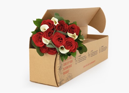 Bouquet of red roses with green leaves elegantly presented in an open cardboard flower box on a neutral background, perfect for gift delivery services.