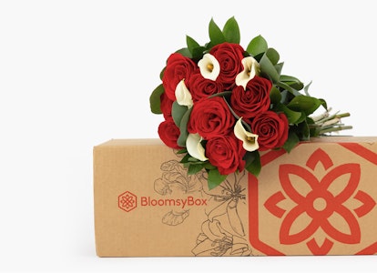Elegant bouquet of red roses and white lilies with lush greenery, packaged in a decorative BloomsyBox, against a neutral background, symbolizing a refined gift.