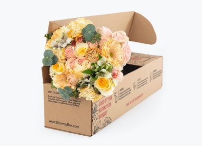 Beautiful bouquet of mixed flowers with roses and eucalyptus leaves emerging from a cardboard delivery box on a white background, symbolizing online floral delivery services.