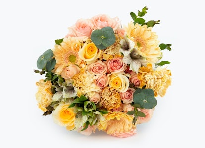 Beautiful floral arrangement with a mix of peach, yellow, and cream flowers, including roses and dahlias, accented with green eucalyptus leaves on a white background.