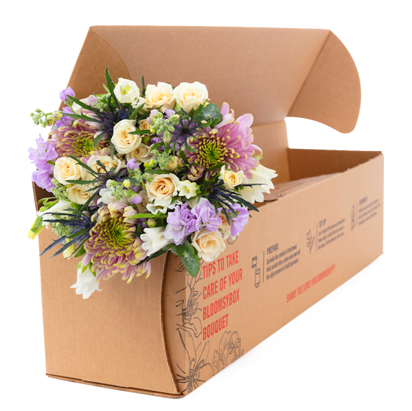 Beautiful bouquet featuring white roses and purple flowers bursting from an open cardboard box marked with care instructions, ready for delivery.