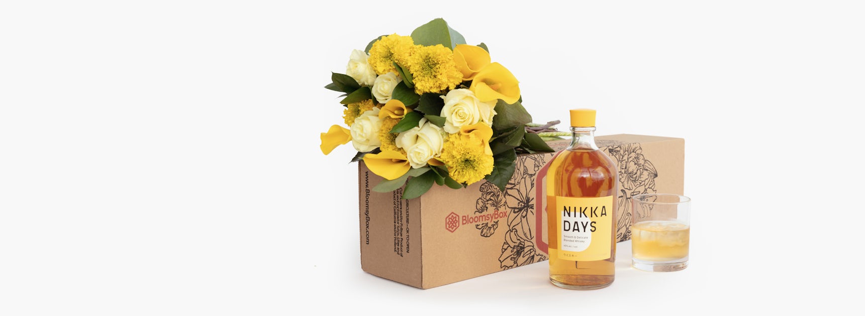 A vibrant gift box featuring a yellow floral arrangement, whiskey, and a glass.