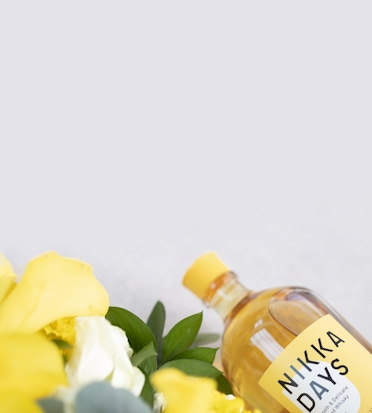 A bottle of Nikka Days whiskey showcased alongside vibrant yellow flowers.