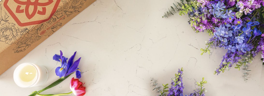 A vibrant assortment of purple and blue flowers, complemented by a candle on a marble surface.