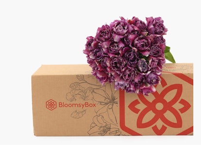 A vibrant bouquet of purple flowers protruding from a BloomsyBox with a floral design, positioned against a clean, neutral background, showcasing fresh flower delivery.