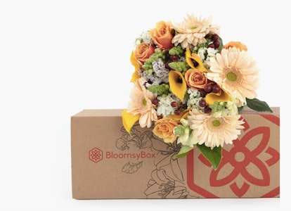 Vibrant bouquet of fresh flowers with roses and daisies spilling from a BloomsyBox, which is partly open and features a red floral logo on a white background.