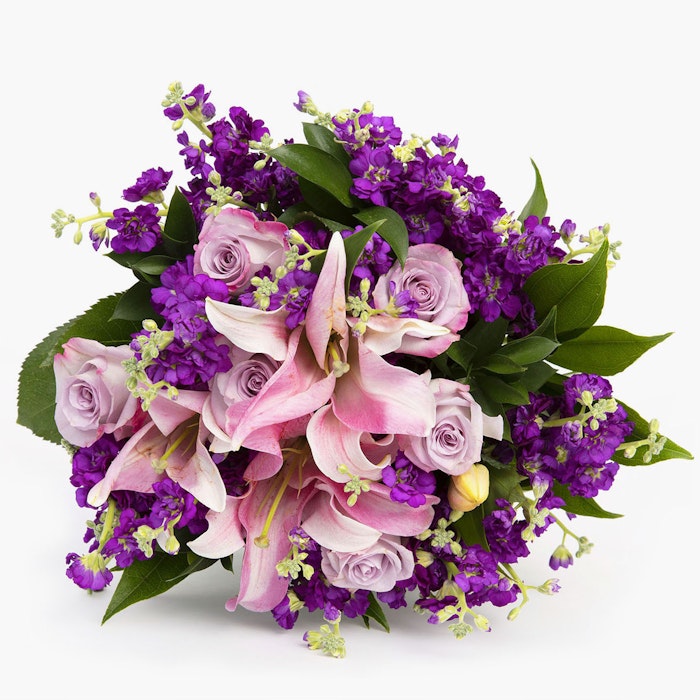 Beautiful bouquet of flowers featuring pink lilies, purple roses, and mixed greenery on a clean white background, ideal for special occasions or as a centerpiece.