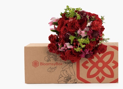 Vibrant bouquet of red roses and assorted flowers emerging from a BloomsyBox with decorative patterns, ideal for special occasions or gifting, on a neutral background.