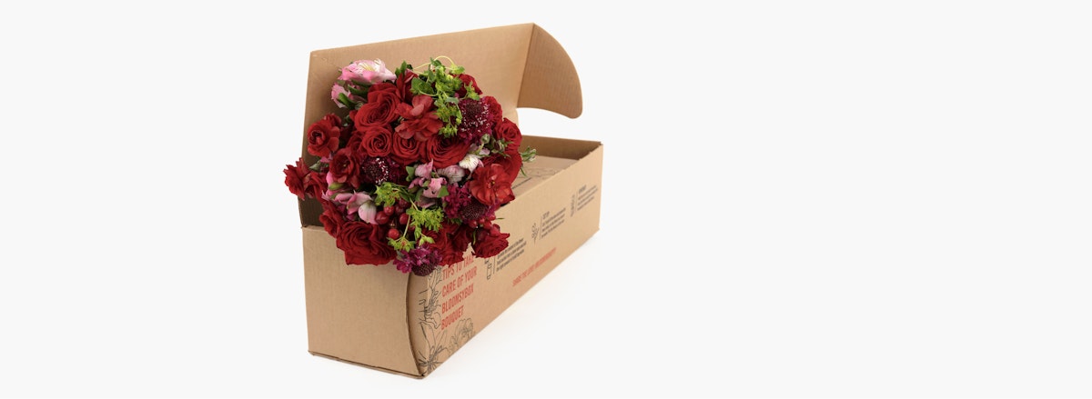 Vibrant bouquet of mixed flowers in rich reds and pinks, elegantly packaged in a kraft box.