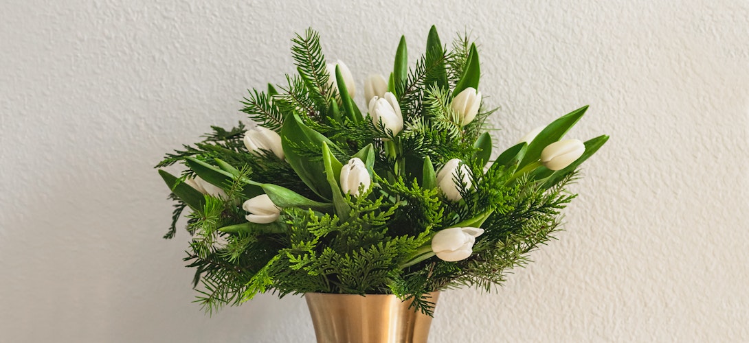 White tulips and lush greenery arranged elegantly in a gold vase, perfect for spring decor.