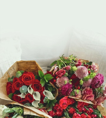 A beautiful arrangement of fresh flowers including red roses, purple blooms, and green foliage wrapped in brown paper against a white background.