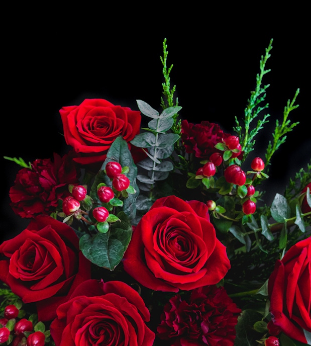 A vibrant bouquet of red roses accented with lush greenery and berries, perfect for gifting.