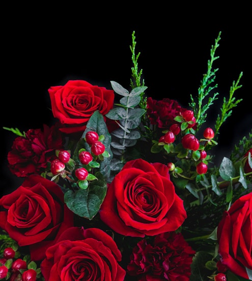 A vibrant bouquet of red roses accented with lush greenery and berries, perfect for gifting.